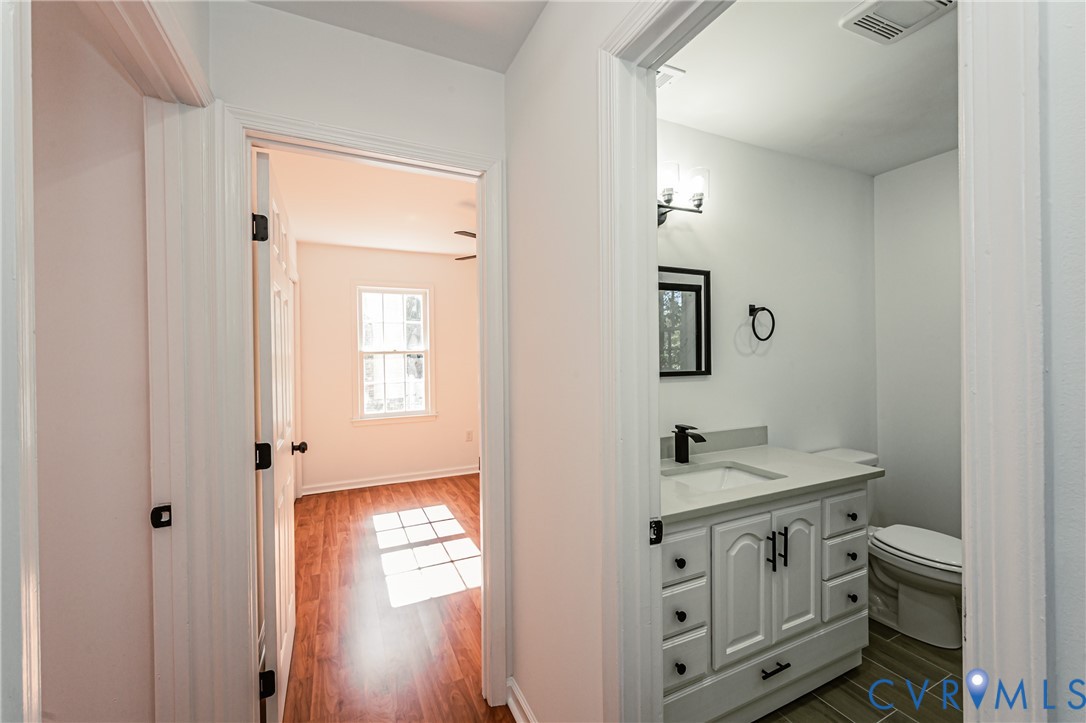 Bathroom featuring a white vanity cabinet with matte black hardware, stone-surface countertop, rectangular undermount sink, and dark-toned floor tiling