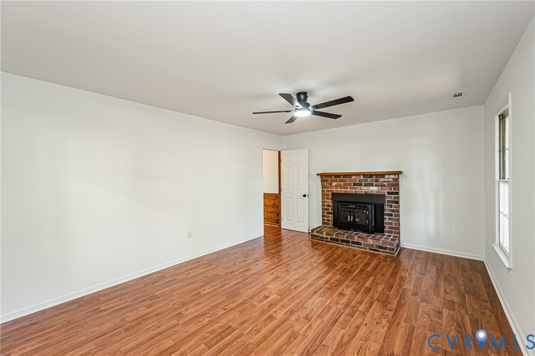Brick fireplace with a wood mantel, wood-finish flooring, and a ceiling fan with integrated lighting