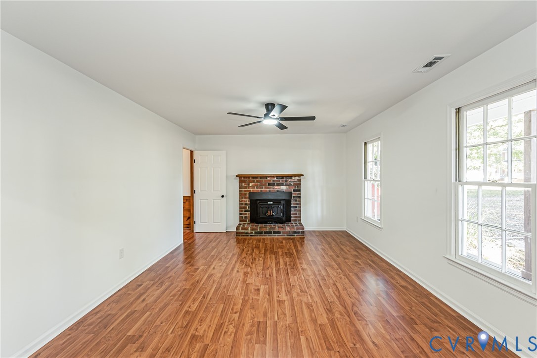 Interior space featuring wood-finish flooring, a red-brick fireplace, a wooden mantel, and a ceiling-mounted light fixture with a fan