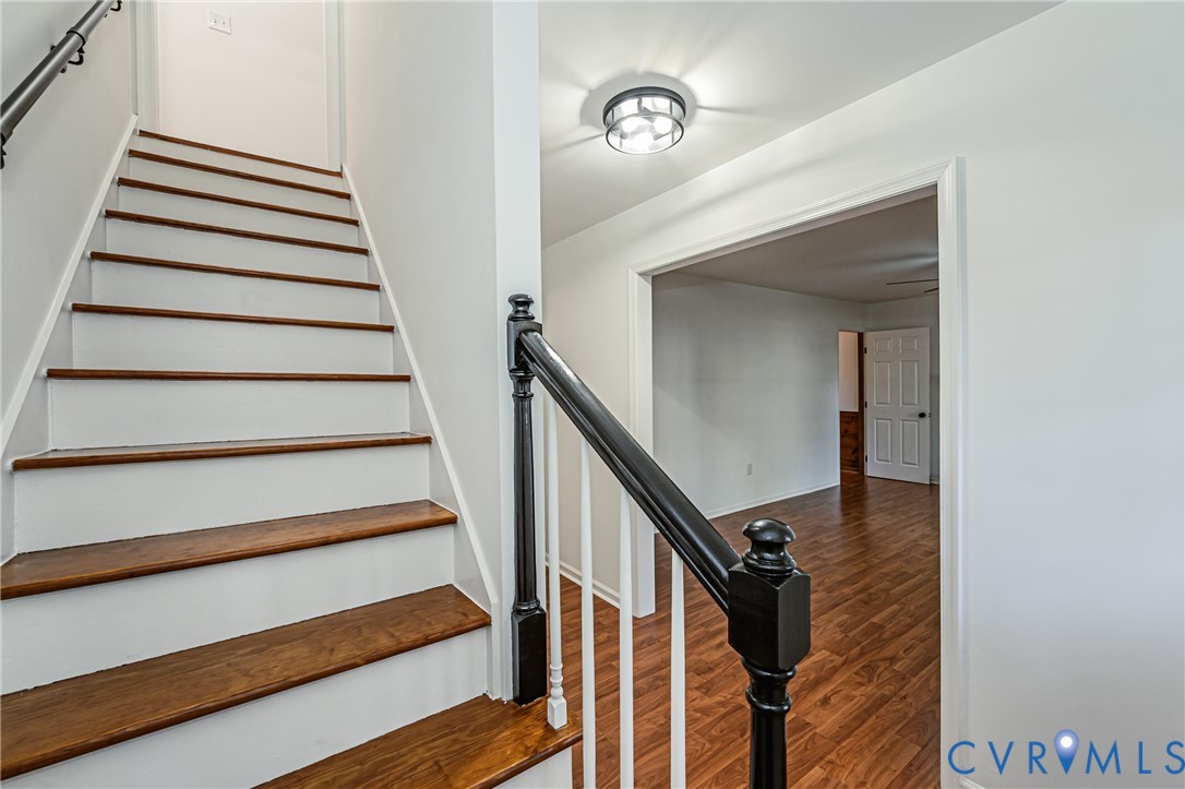 Staircase featuring wood-finish treads, white risers, and a black-finished handrail with white balusters, illuminated by a flush-mount circular ceiling fixture