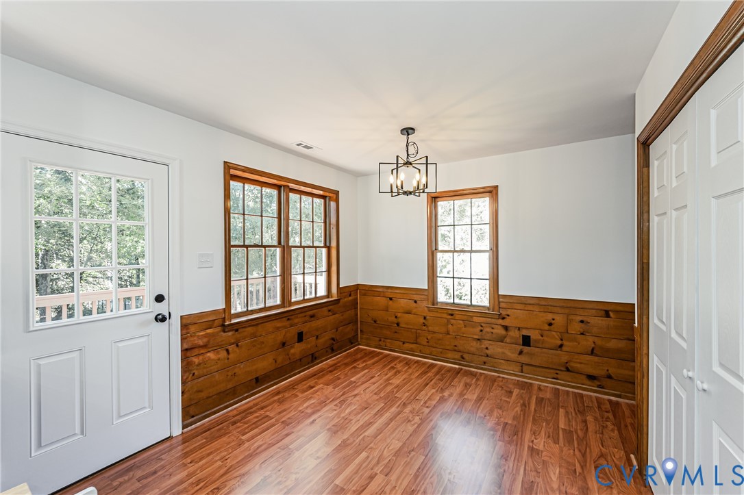 Wood-finish flooring, half-wall wood paneling, multi-pane windows with wood trim, six-pane glass entry door, and a geometric-style metal pendant light fixture