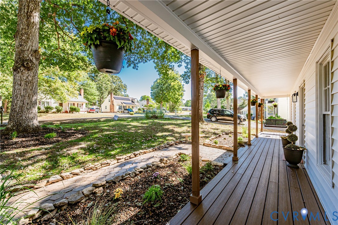 Covered front porch featuring wood-finish decking, horizontal siding, and natural stone border hardscaping