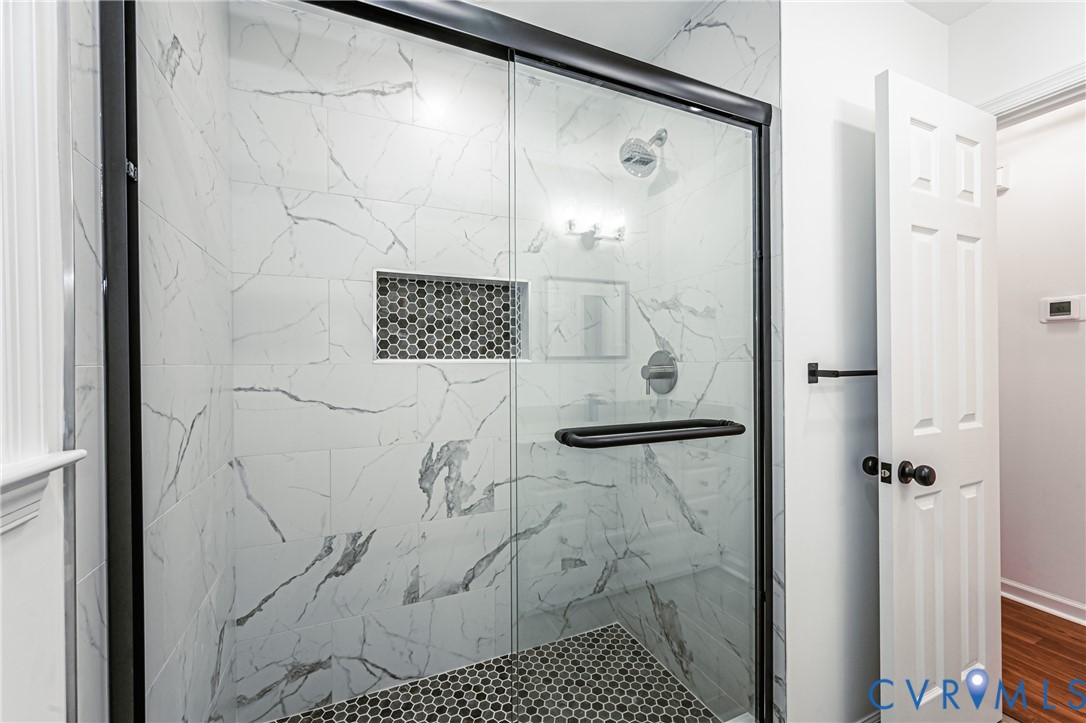 Walk-in shower featuring large-format white veined wall tile, a mosaic tile floor, an integrated wall niche, and a matte black frame glass enclosure