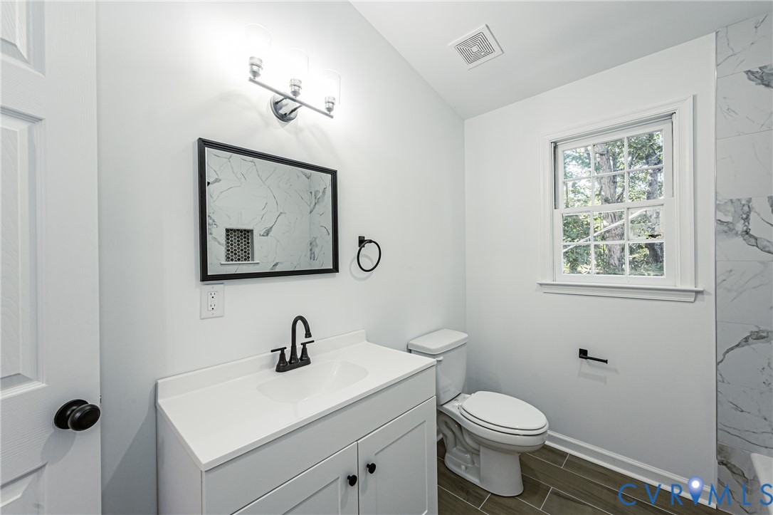 White vanity featuring a solid surface countertop, matte black faucet, framed mirror, and three-light vanity fixture, complemented by tile flooring and tiled wall accents