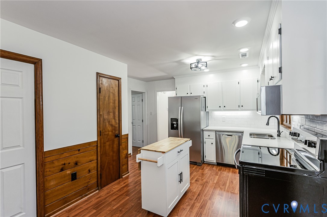 Kitchen featuring white shaker-style cabinetry, stainless steel appliances, wood-finish flooring, and natural wood wainscoting