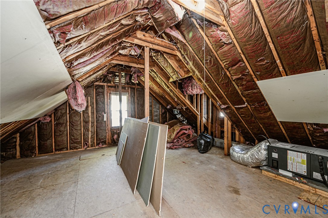 Unfinished attic space featuring exposed wood-frame rafters, fiberglass insulation, subflooring, and an installed HVAC unit