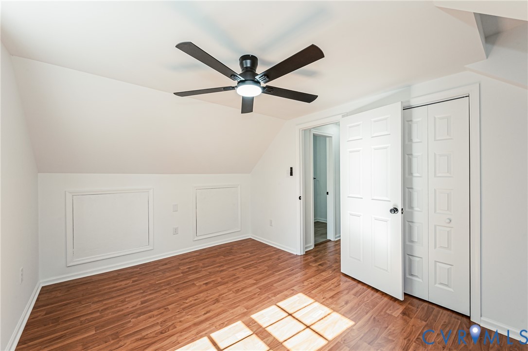 Room featuring wood-finish flooring, a matte black ceiling fan with integrated lighting, dual wall access panels, and white six-panel interior doors