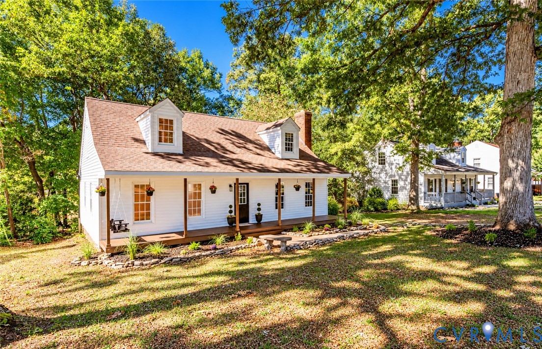 White-sided exterior featuring a covered front porch, dual dormer windows, a brick chimney, and rock-lined landscaping