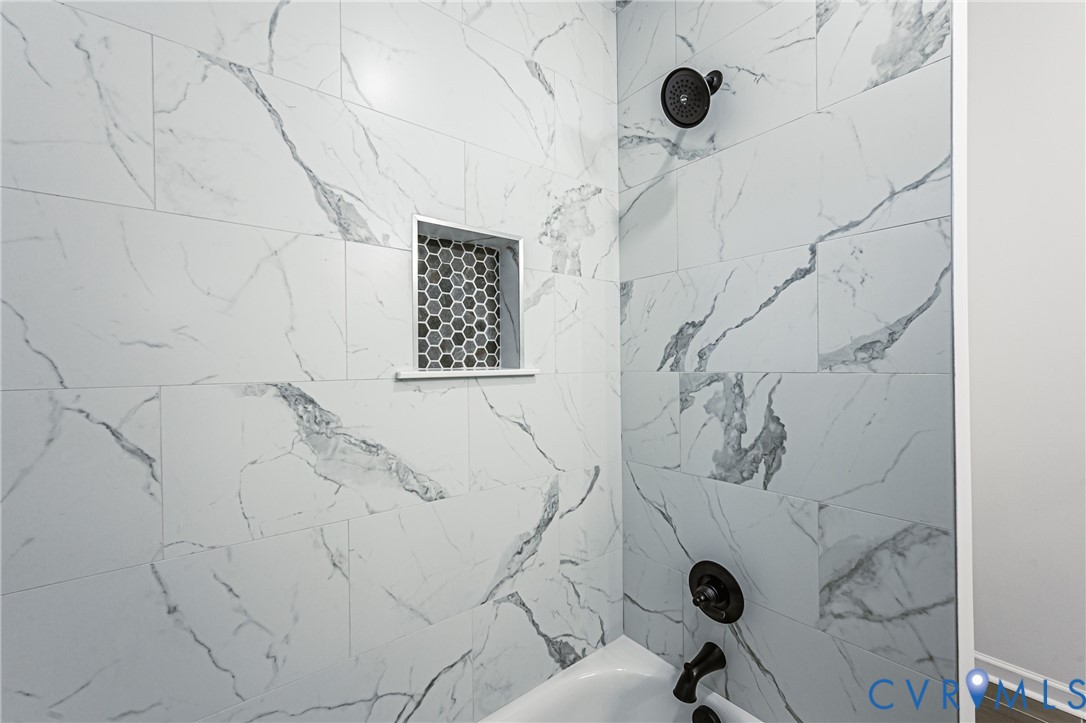 Shower area featuring floor-to-ceiling large-format veined tile, integrated hexagonal tile niche, matte black fixed shower head, and matching matte black wall-mounted faucet controls