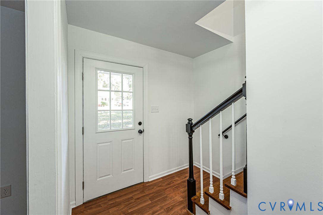 Entryway featuring a white door with a six-pane window insert, wood-finish flooring, and a staircase with white spindles, black handrails, and wood-finish treads