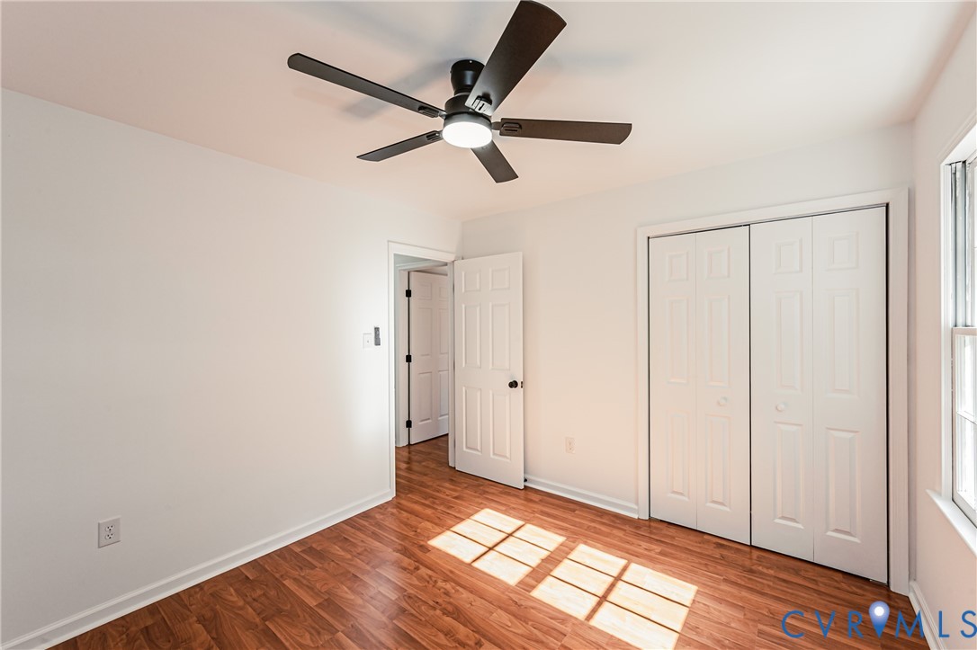Wood-finish flooring, multi-paneled closet doors, six-panel interior door, and a five-blade ceiling fan with integrated lighting