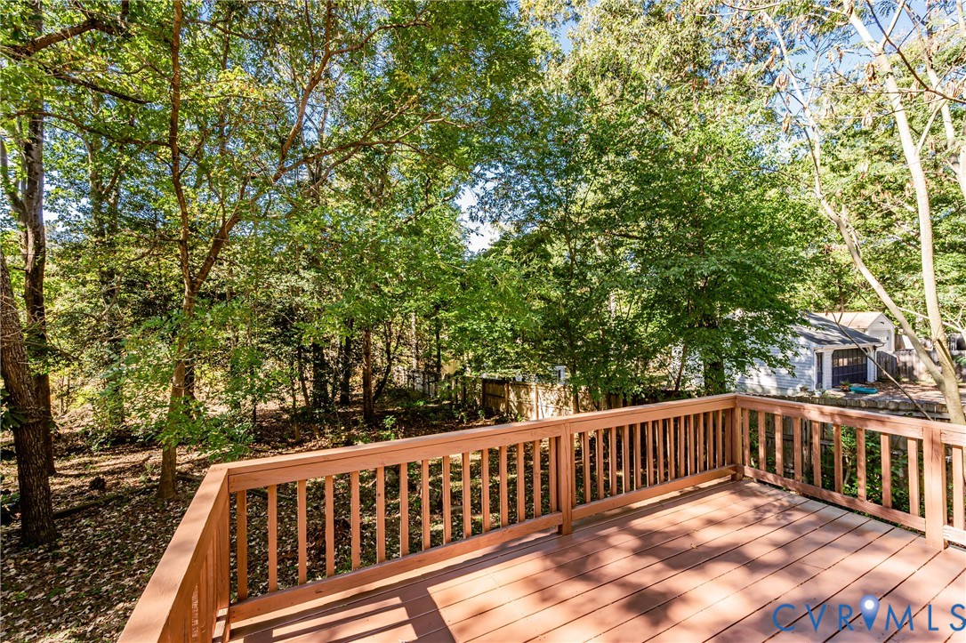 Elevated wood deck featuring vertical slat railings, wood-finish flooring, and mature surrounding trees