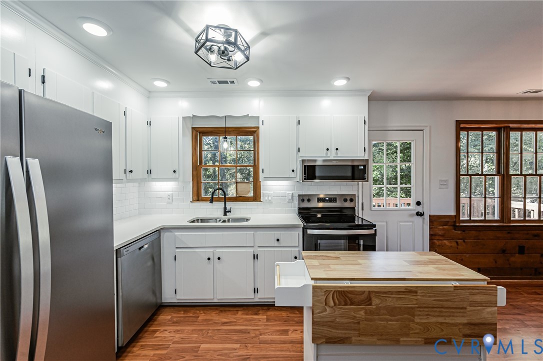 Kitchen featuring white shaker-style cabinetry, stainless steel appliances, subway tile backsplash, wood-finish flooring, and a central island with a wood-block surface