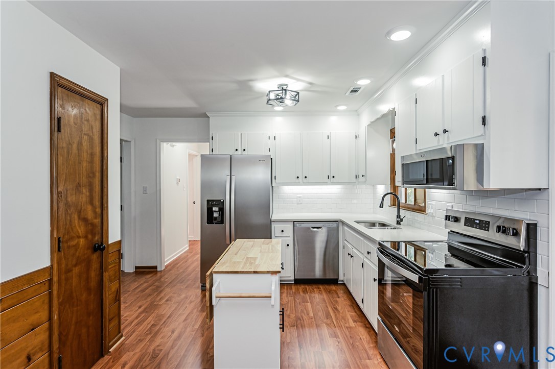 Kitchen featuring white cabinetry, wood-finish flooring, stainless steel appliances, subway tile backsplash, and a butcher block island