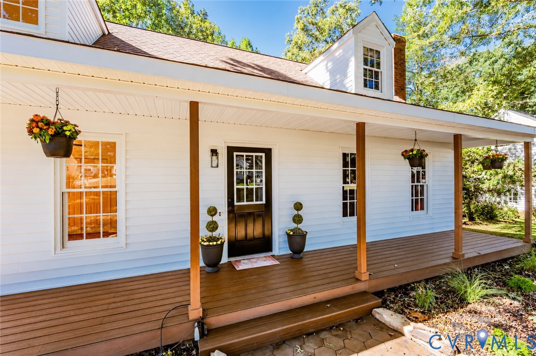 Exterior facade featuring white horizontal siding, a covered front porch with wood-finish decking, dark-toned entry door with grid-pane glass, and roof dormers