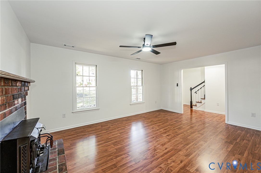 Living area featuring wood-finish flooring, a brick fireplace with a metal insert, multi-pane windows, and a ceiling fan