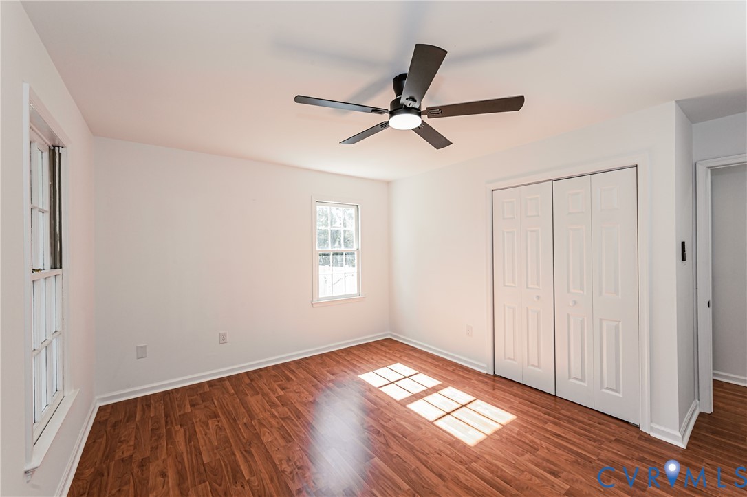 Interior space featuring wood-finish flooring, white walls, dual-panel closet doors, double-hung windows, and a matte black ceiling fan with integrated lighting