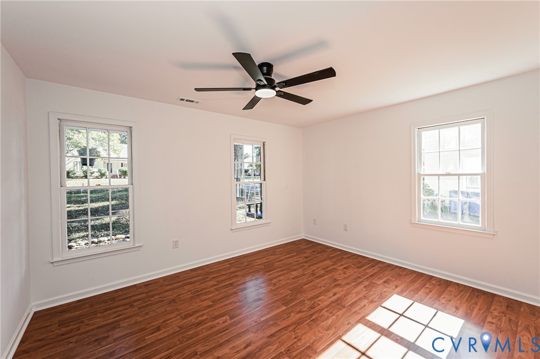 Room featuring wood-finish flooring, three double-hung windows with grid detailing, and a black ceiling fan with integrated lighting