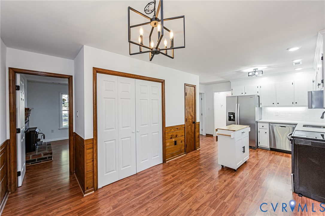 Kitchen featuring wood-finish flooring, half-wall wainscoting, white cabinetry, stainless steel appliances, and a geometric chandelier