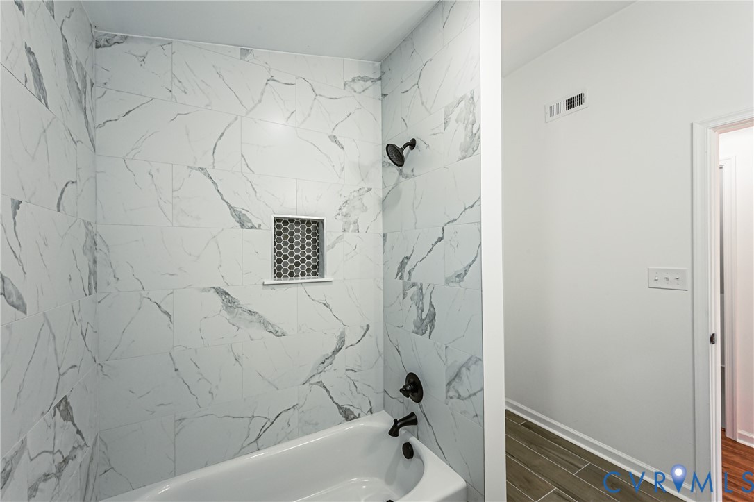 Bathtub with large-format stone-patterned wall tile, matte black hardware, and integrated hexagonal tile shower niche