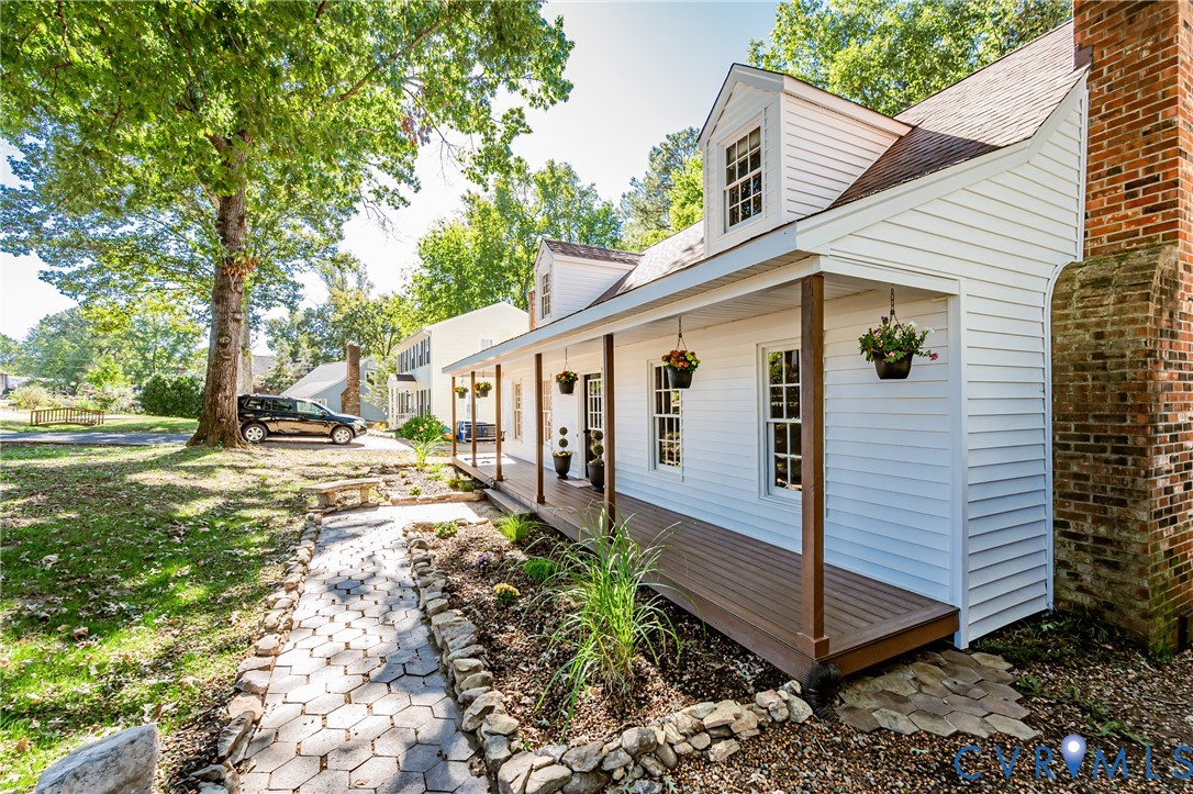 Exterior featuring white siding, a wraparound covered porch with wood-finish decking, two dormer windows, and a prominent brick chimney