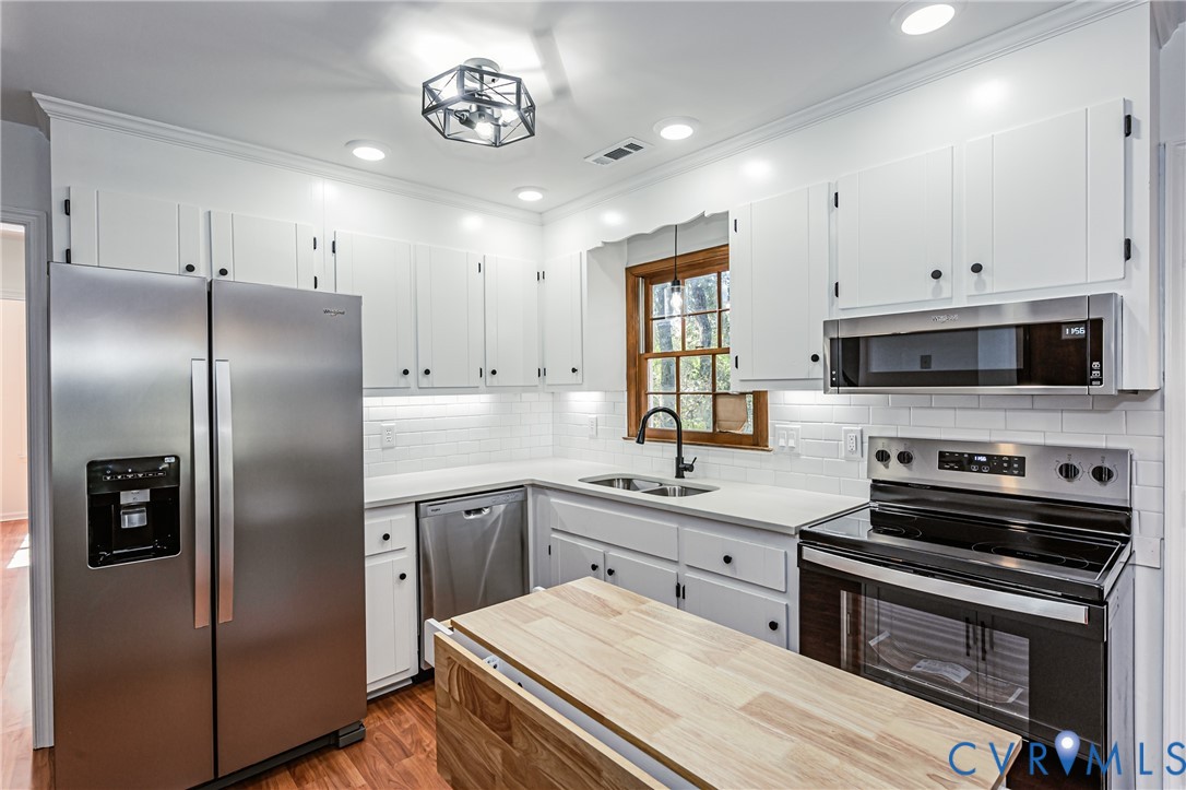 Kitchen featuring white cabinetry, stainless steel appliances, subway tile backsplash, wood-finish flooring, and a butcher block island