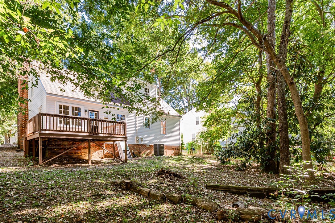 Rear elevation featuring a multi-level wood deck, white vinyl siding, brick foundation, and mature canopy trees