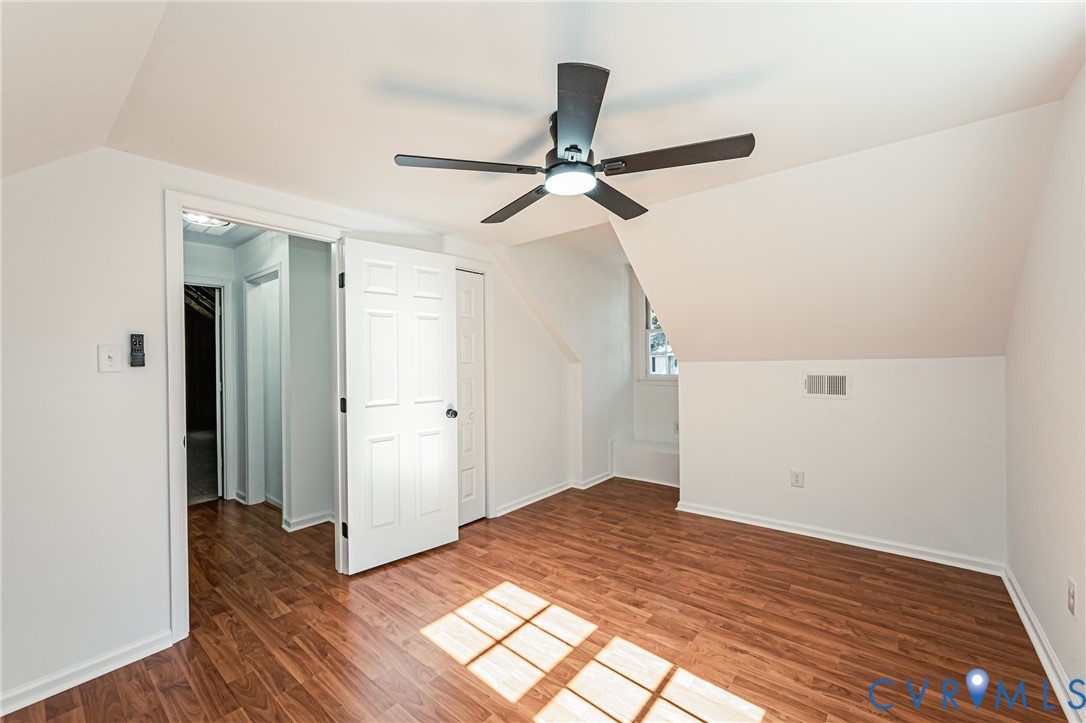 Room featuring sloped ceilings, wood-finish flooring, a six-panel interior door, and a central ceiling fan with integrated lighting