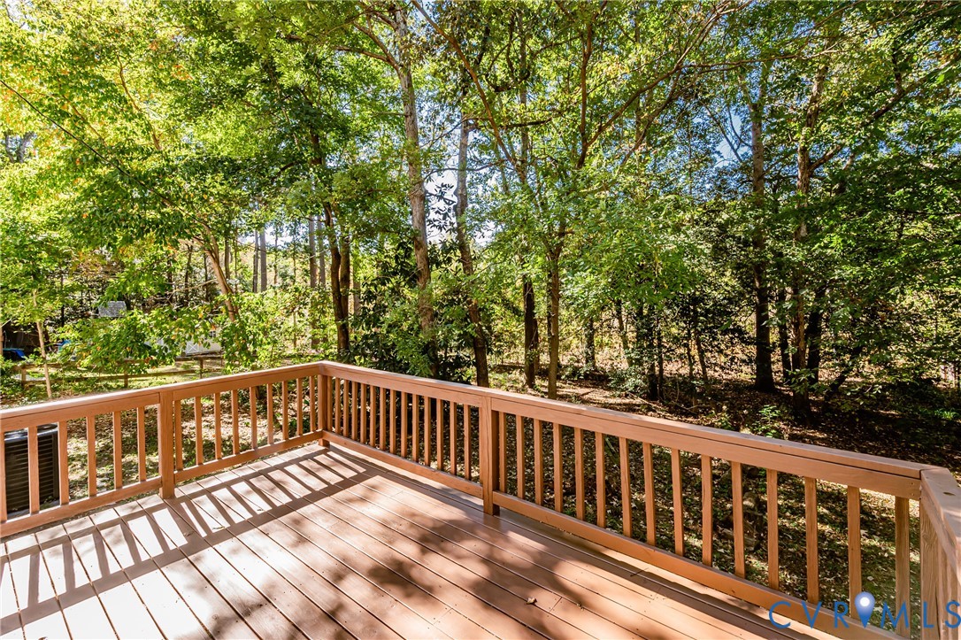 Elevated wooden deck featuring wood-finish flooring, a perimeter railing, and mature tree-lined surroundings