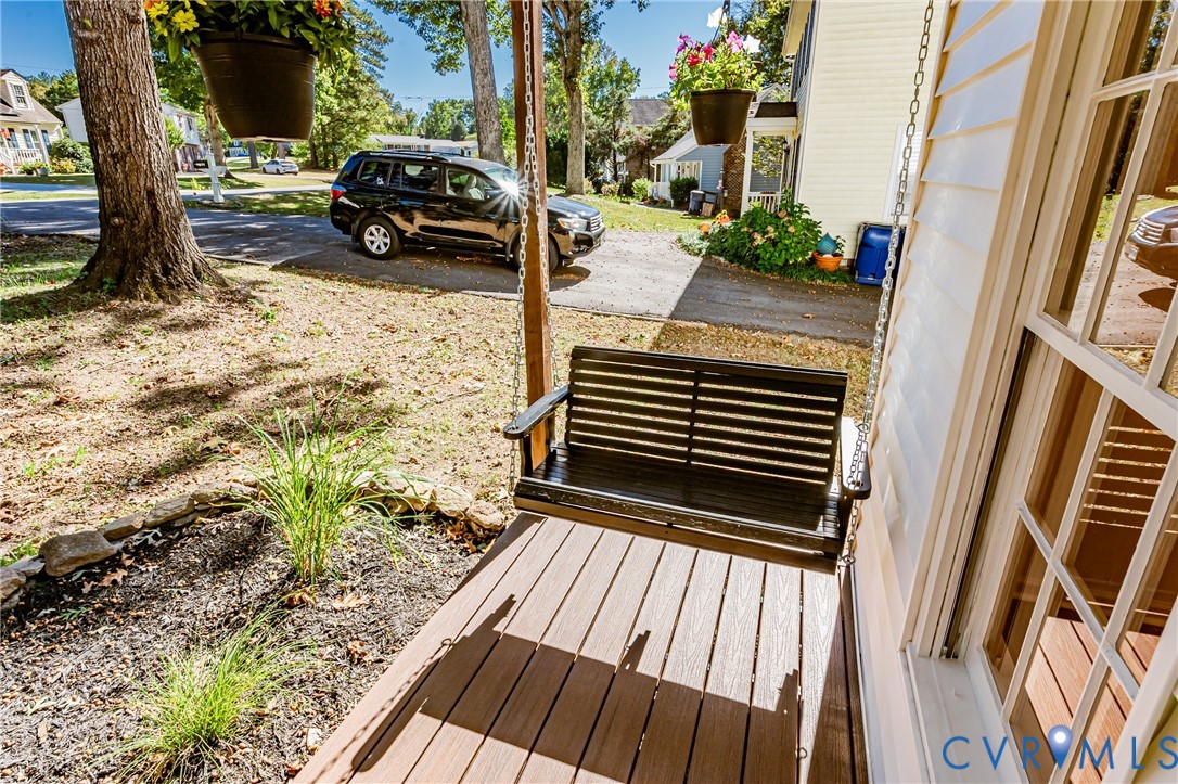 Covered front porch featuring composite decking, a hanging swing, and exterior siding with multi-pane windows