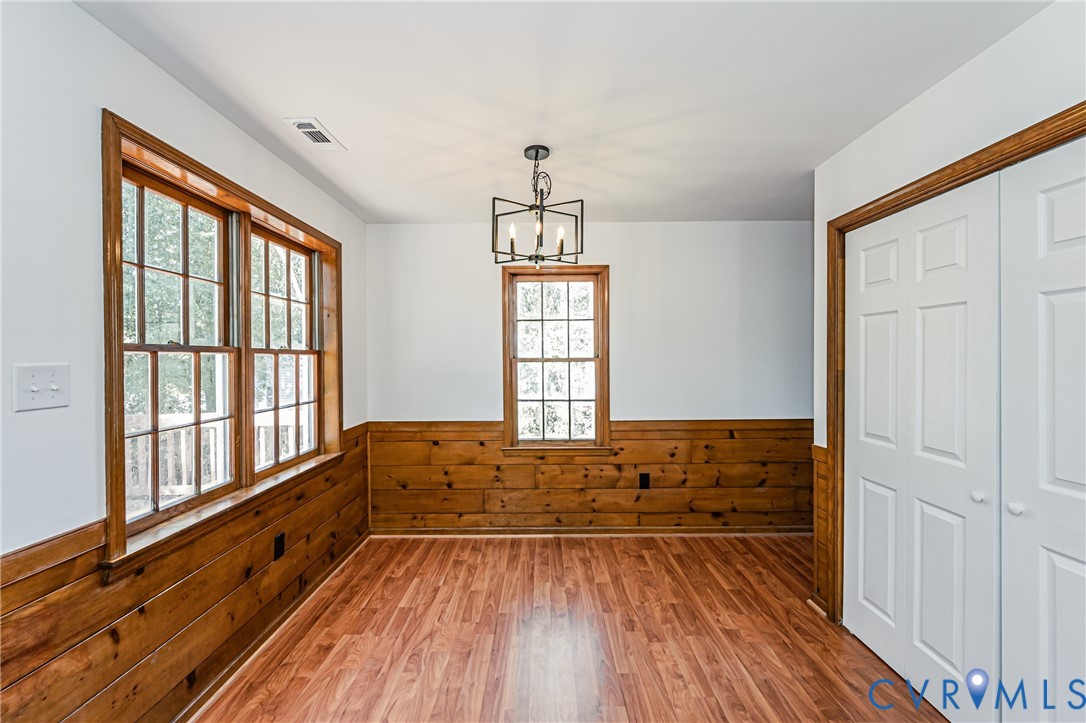 Wood-finish flooring, half-height wood paneling, multi-pane windows with wood trim, six-panel closet doors, and geometric metal chandelier
