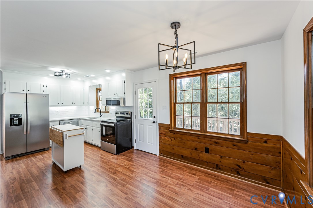 Kitchen featuring white shaker cabinetry, stainless steel appliances, wood-finish flooring, half-wall wood paneling, and a geometric-style metal chandelier