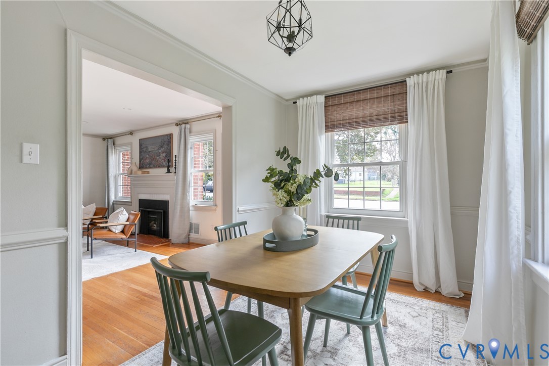 Dining area featuring wood-finish flooring, wainscoting, a geometric pendant light fixture, and multi-pane windows with woven shades