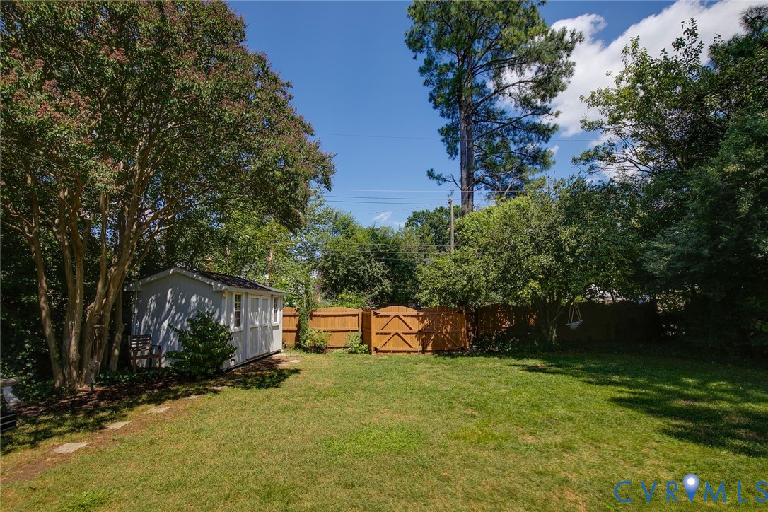 Backyard featuring a grass lawn, wooden privacy fencing, detached storage structure, and mature trees