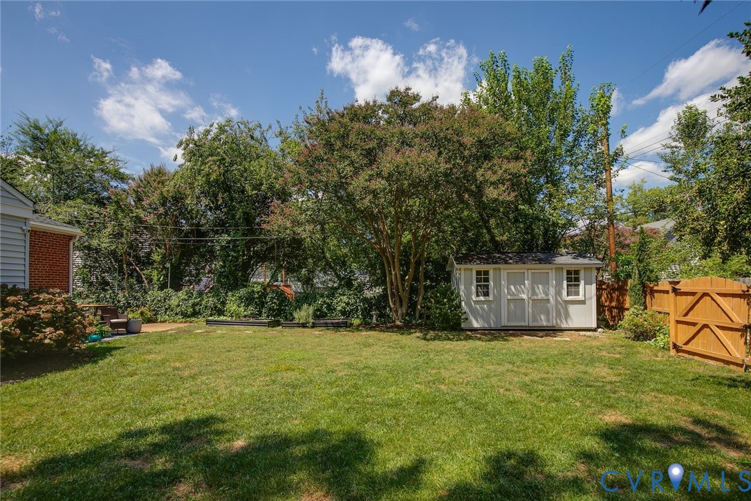 Backyard featuring a grass lawn, mature trees, storage shed, and wood perimeter fencing