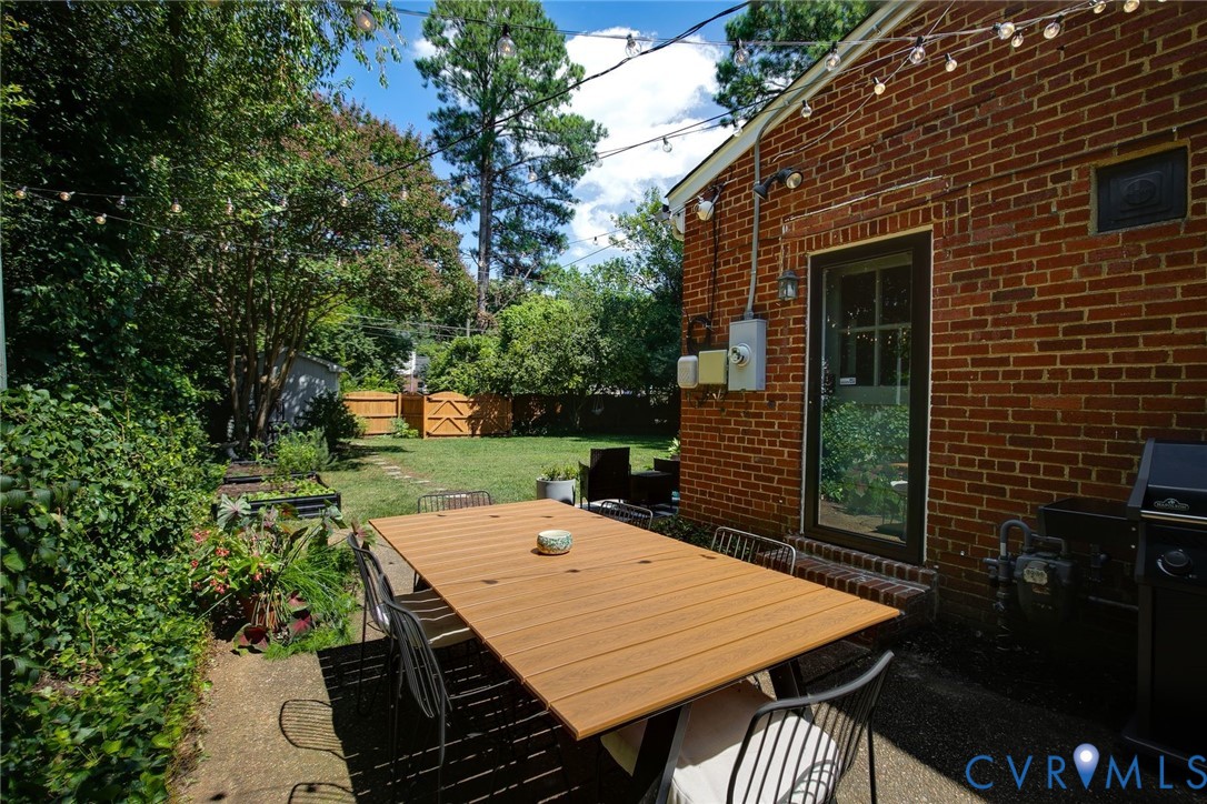 Private backyard featuring a brick exterior wall, concrete patio, perimeter wood fencing, and mature landscaping