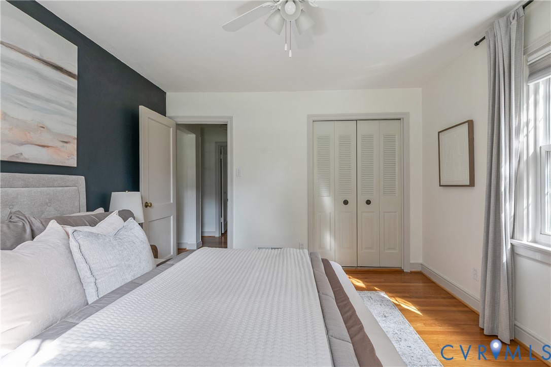 Hardwood flooring, dark-toned accent wall, dual-paneled closet doors, and central ceiling fan with integrated lighting