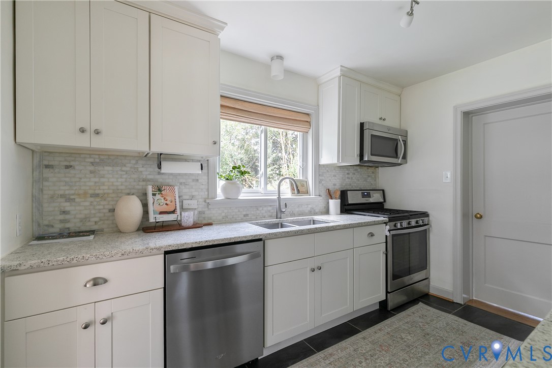 Kitchen featuring white cabinetry, stone-finish countertops, tile backsplash, stainless steel appliances, and dark tile flooring