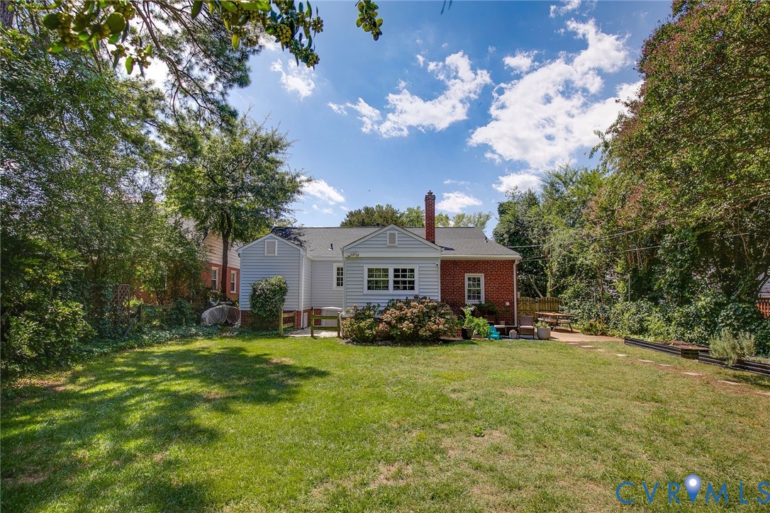 Expansive backyard featuring a manicured lawn, mature trees, brick and siding exterior, and a chimney