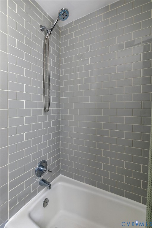 Shower and bathtub combination featuring gray subway tile surround, chrome hand-held shower head, and chrome faucet hardware