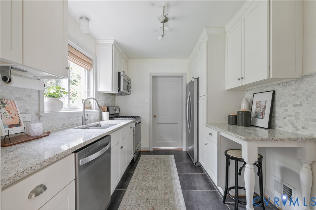 Kitchen featuring white shaker-style cabinetry, stone countertops, a mosaic tile backsplash, stainless steel appliances, and a built-in breakfast bar