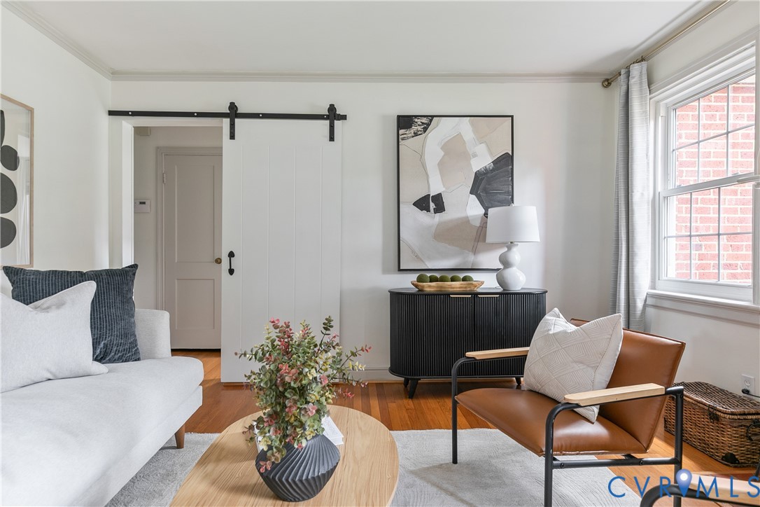 White interior walls with crown molding, wood-finish flooring, and a white sliding barn door with black iron hardware