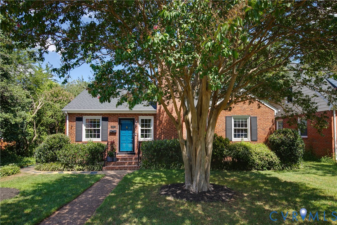 Brick exterior featuring dark shutters, multi-pane windows, a brick chimney, and a paved walkway
