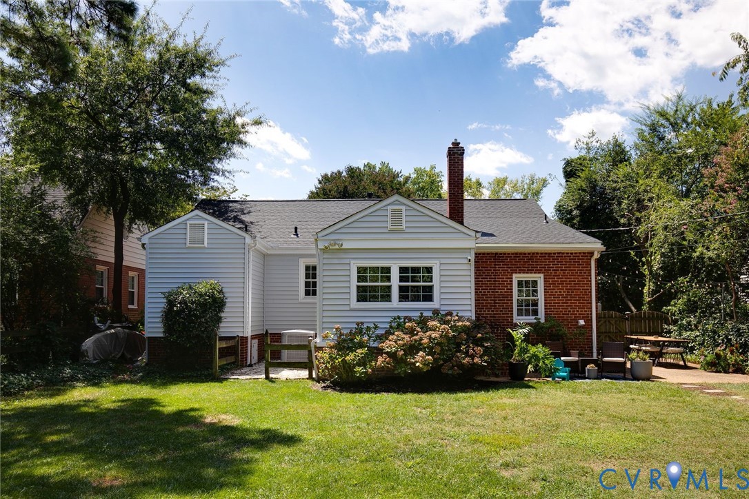 Exterior of home featuring light-colored horizontal siding, red brick accents, an asphalt shingle roof, a masonry chimney, and a stone patio
