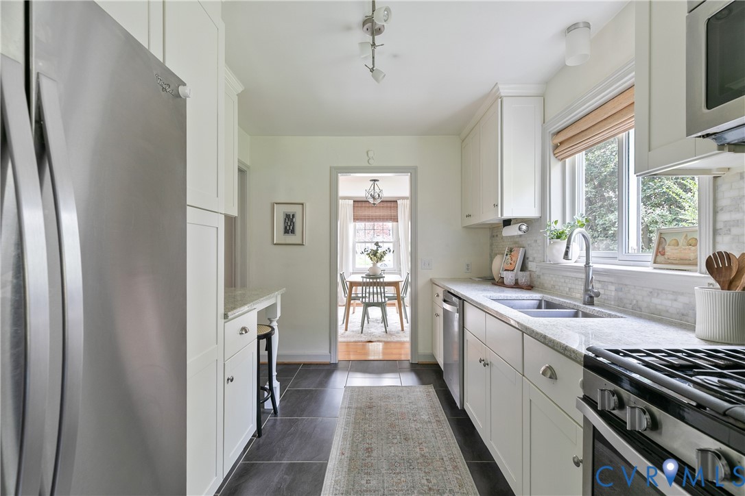 Kitchen featuring white shaker-style cabinetry, stone countertops, stainless steel appliances, a double-basin undermount sink, and tile flooring