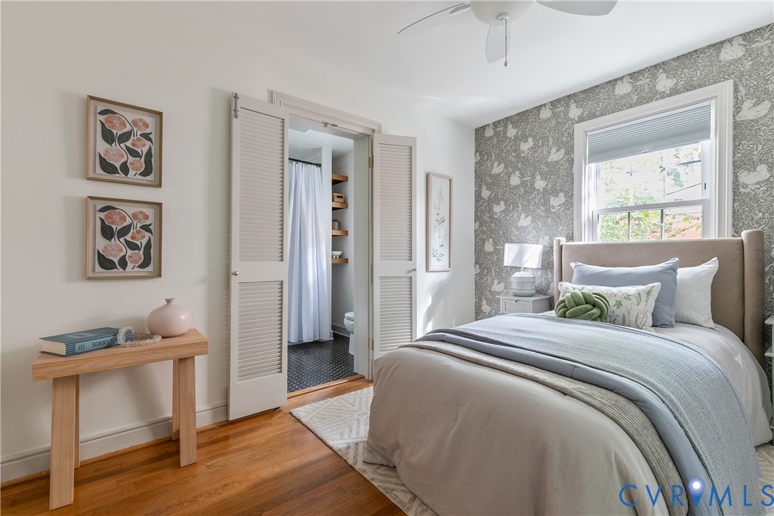 Bedroom featuring wood-finish flooring, patterned accent wallpaper, double louvered closet doors, and an overhead ceiling fan