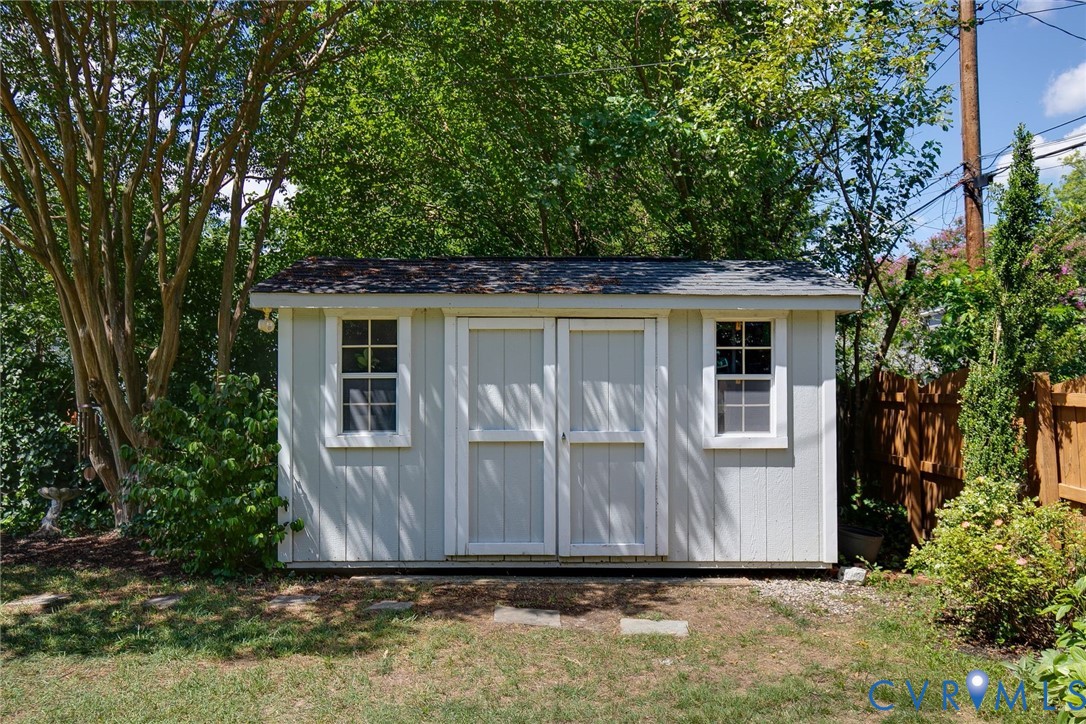 Outdoor storage structure featuring light-toned vertical siding, a shingled roof, double-door entry, and two grid-pane windows