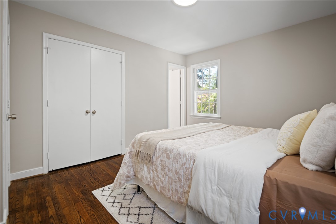 Room featuring wood-finish flooring, double-door closet, neutral wall paint, and a single-hung window with exterior greenery