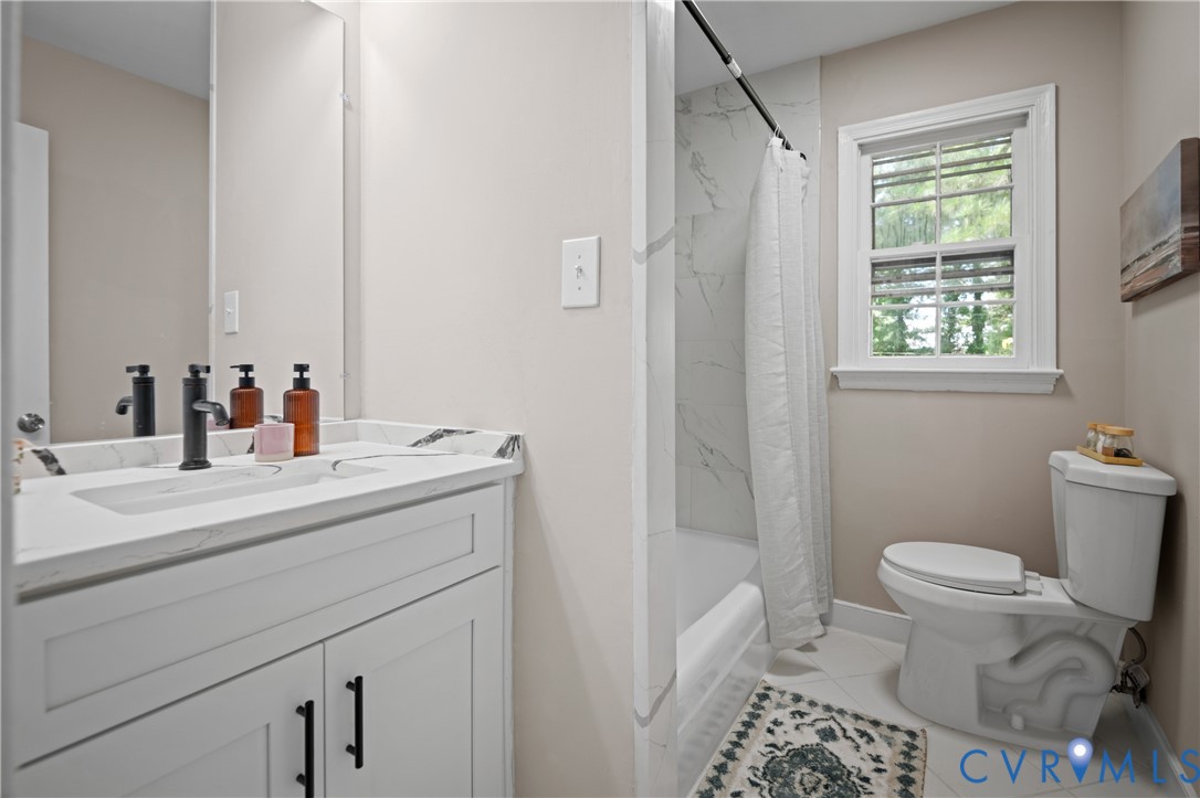 Bathroom featuring a white vanity with a stone-top integrated sink, matte black hardware, large wall-mounted mirror, and a shower-tub combination with white tile surround