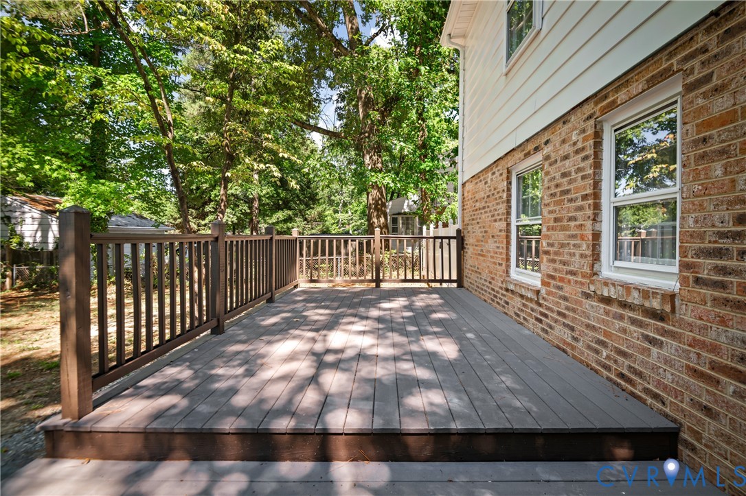 Ground-level composite deck with a dark-toned railing, exterior brick veneer, light-colored horizontal siding, and multiple double-hung windows